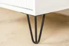 A close-up shot of the bottom corner of a white cabinet with black hairpin legs. Podgląd zdjęcia produktu