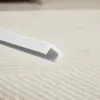A close-up of a white U-shaped plastic profile against a textured light background. Voir les images du produit