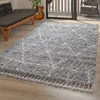 A shaggy rug with a diamond pattern is placed on a wooden floor in a living room setting, with a sofa and a guitar visible in the background. Produktbild-Vorschau