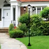 A black metal lamp post with three lights stands in front of a house entrance with a stone pathway and green grass. Produktbild-Vorschau