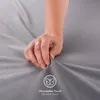 A hand is shown pressing into a soft, gray fabric, likely a bedsheet or textile product. Produktbild-Vorschau