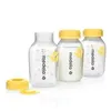 Three Medela baby bottles with yellow caps are displayed on a white background. One bottle contains milk, while the other two are empty. A yellow cap and ring are also shown separately in the foreground. Anteprima dell’immagine prodotto