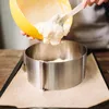 A person is pouring cake batter from a yellow bowl into a stainless steel cake ring. Podgląd zdjęcia produktu