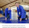 Two people in blue work uniforms are kneeling on a large blue tarp in a warehouse setting. Produktbild-Vorschau