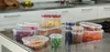 A collection of clear plastic food storage containers filled with various food items, arranged on a stainless steel kitchen counter. Produktbild-Vorschau