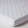 A close-up, angled view of a white quilted mattress topper on a white mattress. Anteprima dell’immagine prodotto