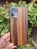 A hand holding a phone with a wood-grain skin, surrounded by green plants. Produktbild-Vorschau
