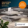 A modern, multi-tiered coffee table in a living room setting with a sofa in the background. Produktbild-Vorschau