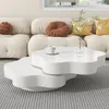 A white, multi-tiered coffee table sits on a striped rug in front of a plush, cream-colored sectional sofa with decorative pillows. Voir les images du produit