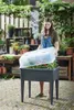 A woman is placing a transparent lid on a raised garden bed filled with plants. Náhled obrázku produktu