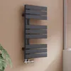 A modern anthracite radiator mounted on a light brown wall, with a plant in the foreground and a window in the background. Produktbild-Vorschau