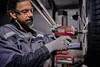 A man is using a cordless impact wrench to tighten a bolt on a car wheel in a workshop. Produktbild-Vorschau