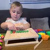A young boy is playing with a wooden bead sorting toy on a table. Voir les images du produit