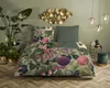 A bedroom scene with a bed dressed in floral bedding, plants, and decorative wall art. Náhled obrázku produktu