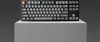 A black mechanical keyboard with gray and orange keys is displayed on a light gray cube against a dark gray background. Produktbild-Vorschau