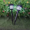 Two solar garden lights are placed in a garden setting with green grass and artificial plants. Anteprima dell’immagine prodotto