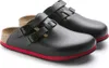 A pair of black Birkenstock clogs with red soles, shown from a diagonal angle on a white background. Anteprima dell’immagine prodotto