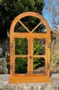 A rusty metal window decoration with an arched top and two doors, set against a blurred background of trees and sky. Produktbild-Vorschau