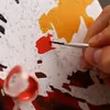 A close-up of a person's hand painting a "paint by numbers" kit. Produktbild-Vorschau