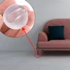 A close-up of a transparent silicone furniture leg protector being held in a hand, with a sofa and its legs visible in the background. Podgląd zdjęcia produktu