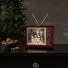 A festive Christmas decoration in the shape of a retro television set, placed on a dark dresser next to a bowl of nuts and a Christmas tree in the background. Podgląd zdjęcia produktu