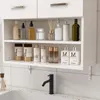 A white bathroom wall cabinet filled with various toiletries and bottles, mounted above a sink with a black faucet. Náhled obrázku produktu