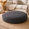 A dark gray round floor cushion is placed on a beige rug in a living room setting, with a white sofa and decorative elements in the background. Produktbild-Vorschau