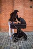A woman is tending to a baby stroller in front of a brick wall. Náhled obrázku produktu
