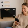 A woman is using a smartphone while sitting on a couch next to a black electric heater. Anteprima dell’immagine prodotto