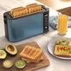 A blue toaster with four slices of toast is shown on a kitchen counter, with a glass of orange juice, toast with avocado and tomatoes, and a bowl of guacamole. Podgląd zdjęcia produktu