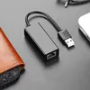 A black USB to Ethernet adapter is placed on a dark gray surface, next to a brown leather object. Voir les images du produit