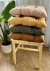 Four colorful cushions are stacked on a wooden chair next to a large potted plant. Produktbild-Vorschau