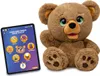 A plush teddy bear is shown next to a tablet displaying a story selection app. Produktbild-Vorschau