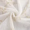 A close-up of white sheer fabric with a gold floral pattern. Produktbild-Vorschau