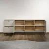 A lowboard cabinet with open compartments and drawers, placed against a white wall on a wooden floor. Produktbild-Vorschau