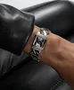 A close-up shot of a woman's wrist wearing a silver Guess watch with a black face. Náhled obrázku produktu
