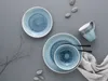 A set of blue stoneware dishes and a mug are arranged on a gray surface, with a few small stones and a dried plant sprig. Náhľad obrázku produktu