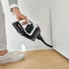 A person is holding a cordless vacuum cleaner and cleaning a corner. Produktbild-Vorschau