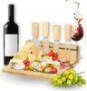 A cheese board set with various cheeses, meats, grapes, tomatoes, and cheese knives, along with a bottle of red wine and a splash of wine in a glass. Produktbild-Vorschau