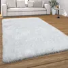 A fluffy white rug is placed on a wooden floor in front of a modern white sofa.