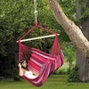 A woman relaxing in a striped hammock chair hanging from a tree in a garden. Náhled obrázku produktu