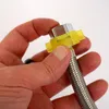 A person's hand is holding a metal hose with a yellow plastic fitting attached to one end. Produktbild-Vorschau