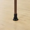 The bottom part of a brown wooden pole with a black adjustable base, resting on a light wooden floor. Náhľad obrázku produktu
