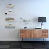 A modern living room with a wooden sideboard, a lamp, a plant, and floating bookshelves on the wall. Produktbild-Vorschau