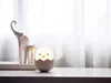 A small, egg-shaped chick night light sits on a white surface in front of a sheer white curtain. Two white elephant figurines are visible in the background. Produktbild-Vorschau