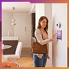 A woman is interacting with a smart home device mounted on a wall in a modern home setting. Podgląd zdjęcia produktu
