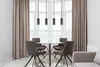 A dining set with a glass table and four chairs, illuminated by pendant lights, in a room with curtains. Podgląd zdjęcia produktu