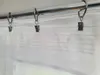 A close-up view of a white sheer curtain hanging from a metal rod with clip rings. Produktbild-Vorschau