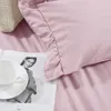 A close-up of a pink duvet cover with a ruffled edge, next to a white teacup and saucer on a magazine. Podgląd zdjęcia produktu