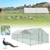 A large outdoor chicken coop with a covered roof section, situated in a grassy field with a few houses in the background. A peacock is shown in the foreground. Produktbild-Vorschau